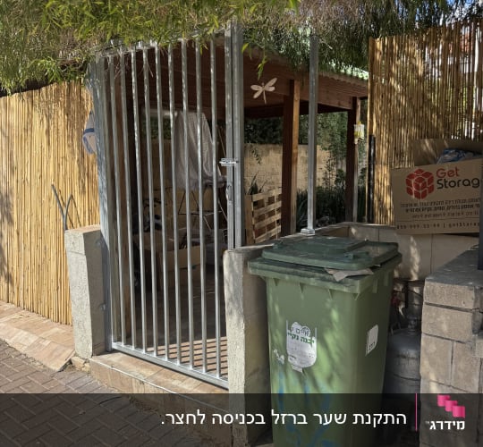 שער מתכת ליד פח אשפה ירוק